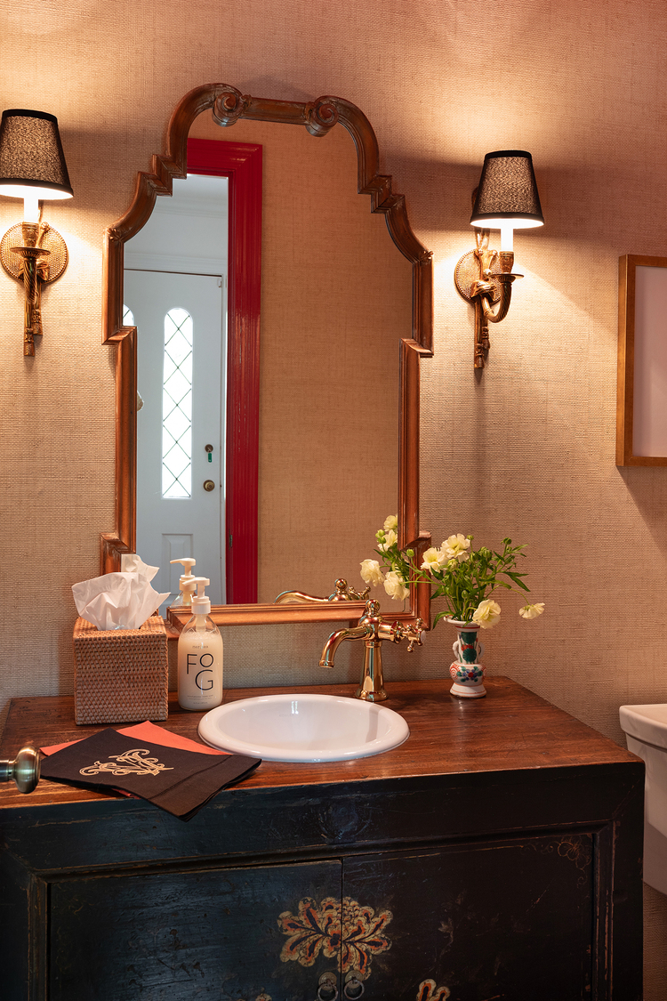 Warm, dramatic bathroom with vintage mirror, intricate sconces, and a deep brown vanity. 