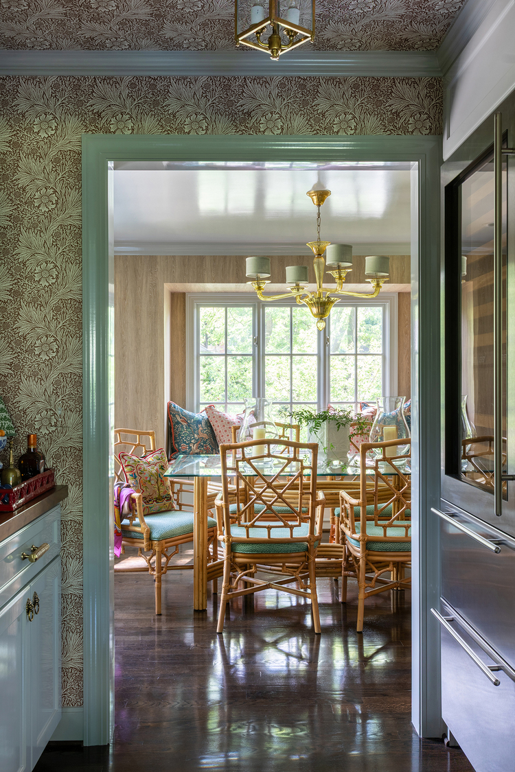 Dining area viewed from the bar, including glass-top table, a golden chandelier, and a large windowseat.