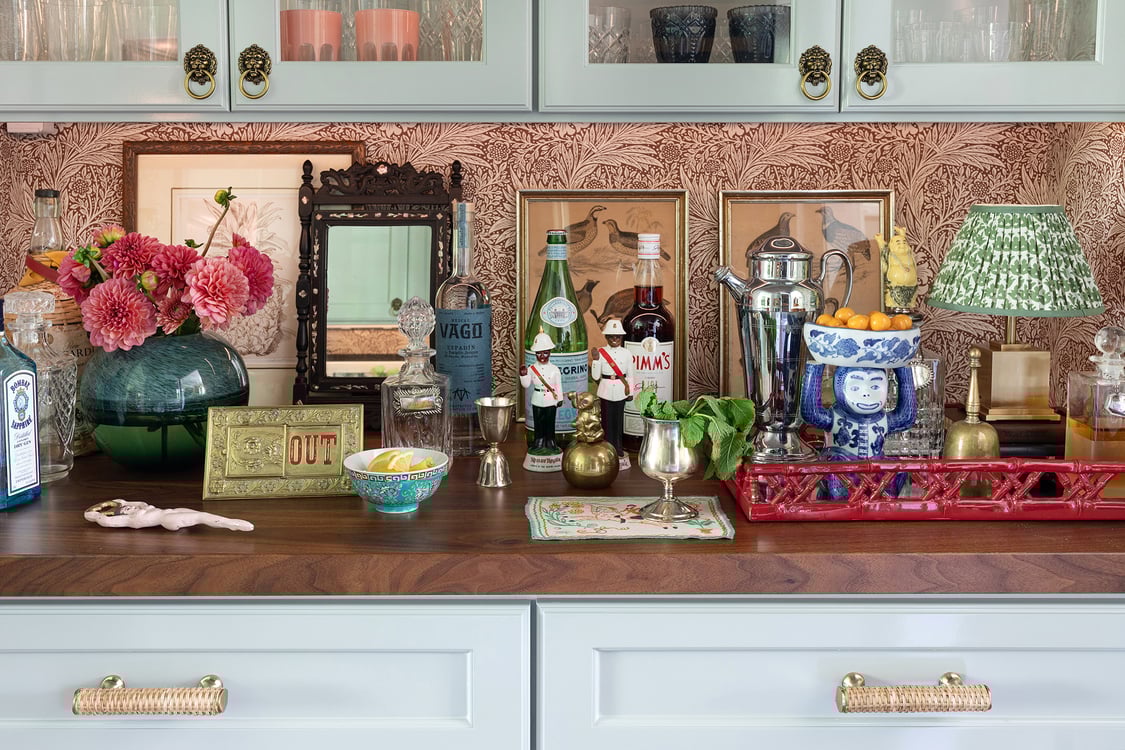 Close-up of the walnut bartop featuring vintage prints, figurines, a small lamp, and a miniature antique mirror.